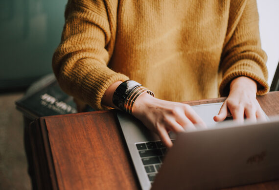 a girl wearing a knitted sweater typing on her laptop
