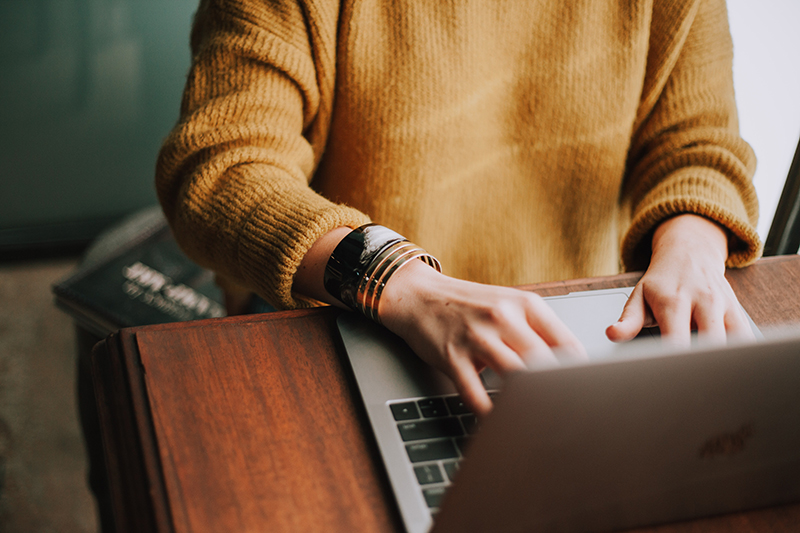 a girl wearing a knitted sweater typing on her laptop