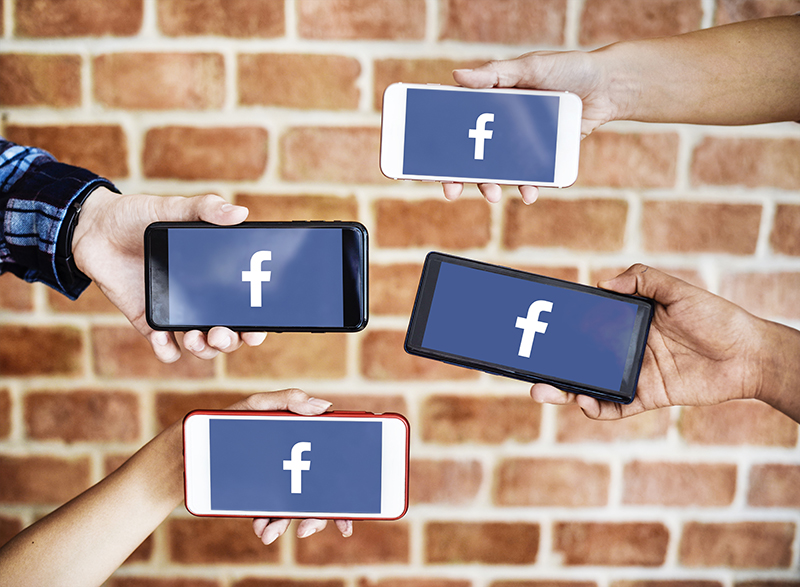 four persons holding smartphones with Facebook icon on each screen