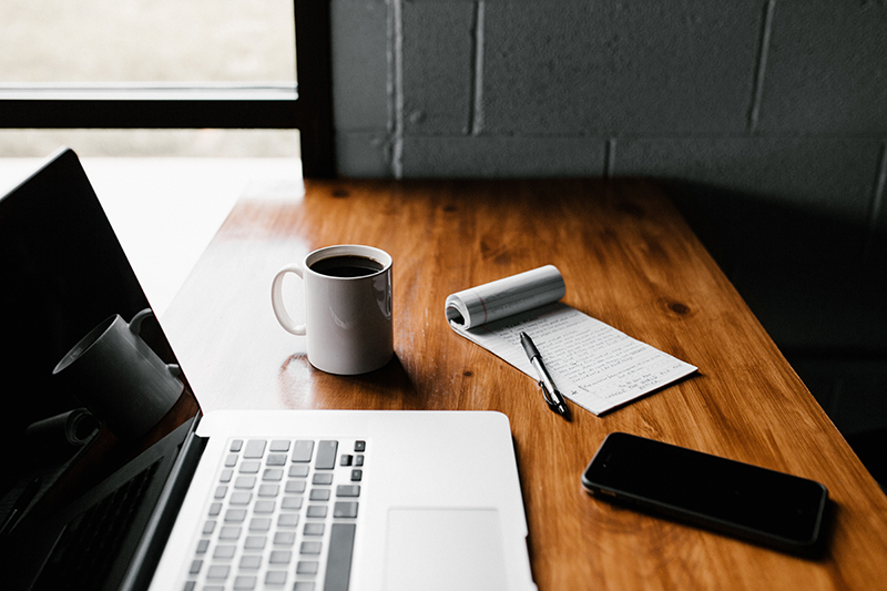 MacBook pro, white ceramic mug, and black smartphone on table