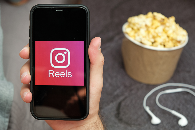 Close up mans hand holding a mobile phone with Instagram Reels logo