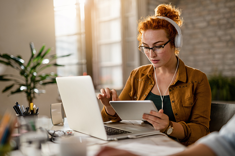 Young creative businesswoman working on digital tablet while wearing headphones in the office.