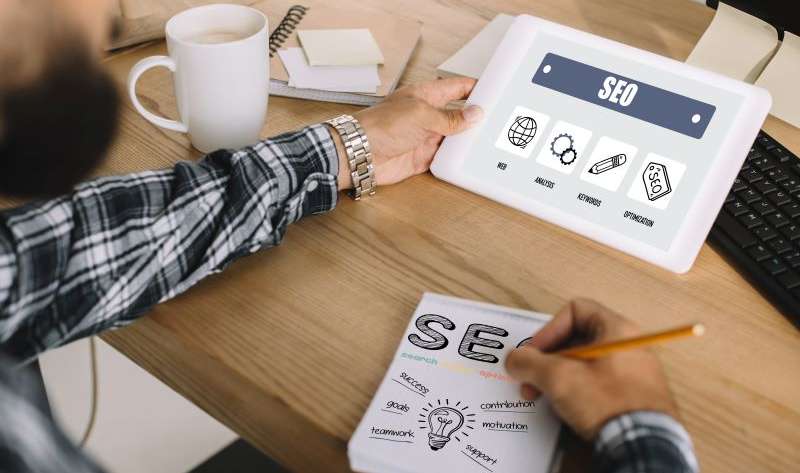 cropped shot of professional seo manager using tablet and writing notes at workplace