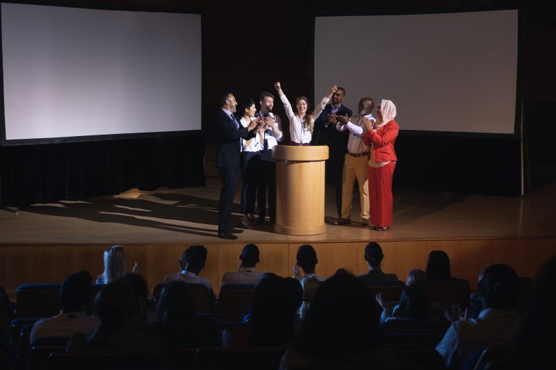 Happy businesswoman standing at the stage of the auditorium with colleagues in front of audience